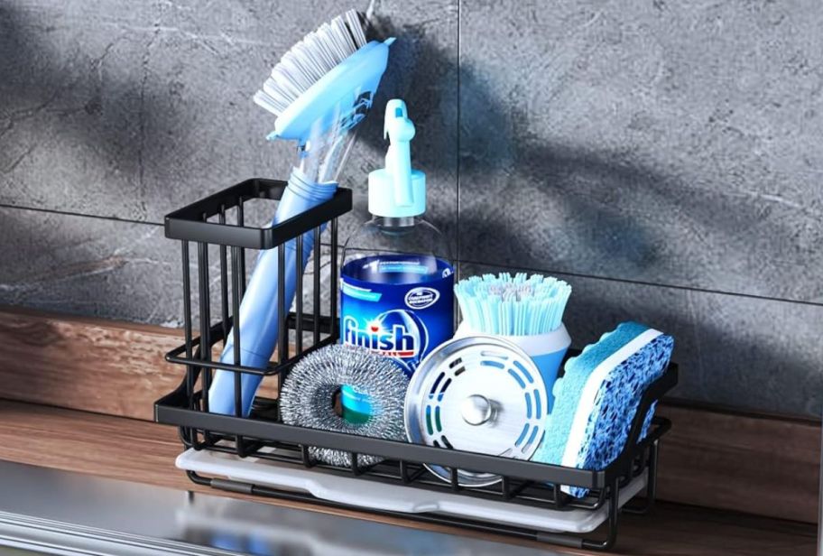 a black steel sink caddy with sponge, dish soap and scrubbers on a counter by a sink