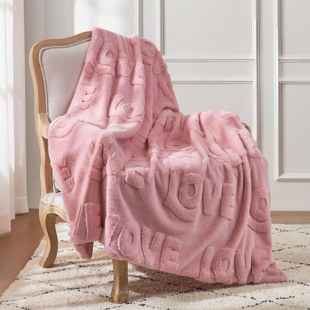 a pink cozy bliss love blanket draped over a white side chair