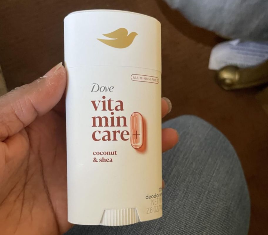 a womans hand holding a tube of dove deodorant in coconut shea scent
