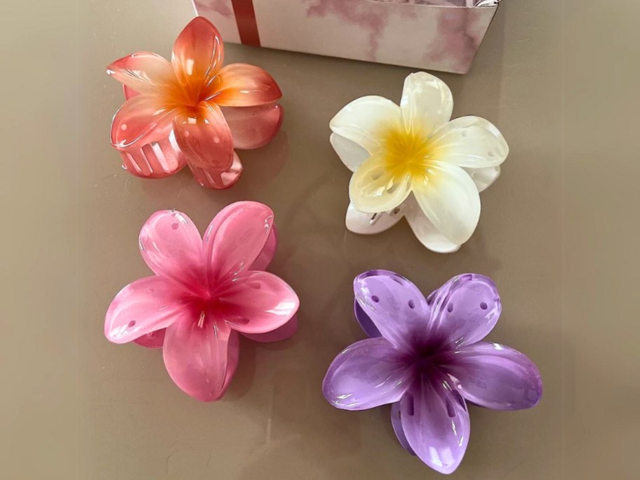 four different color hibiscus flower hair claw clips laying on a table