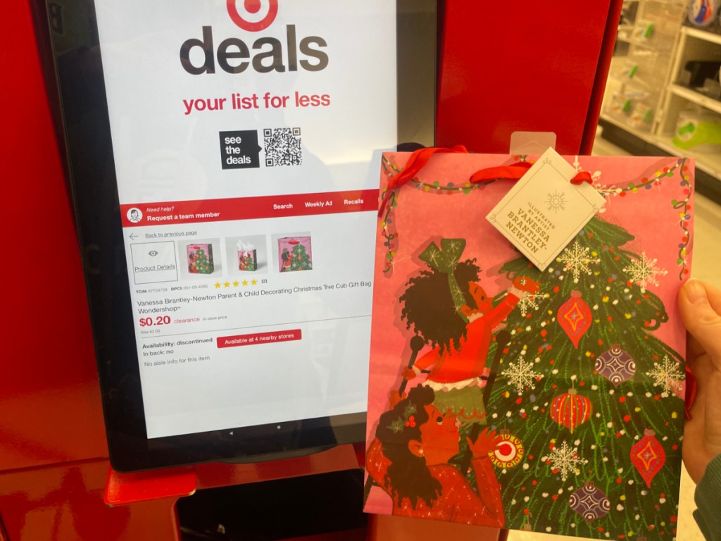 hand holding Vanessa Brantley-Newton Parent & Child Decorating Christmas Tree Cub Gift Bag in front of the price check at Target