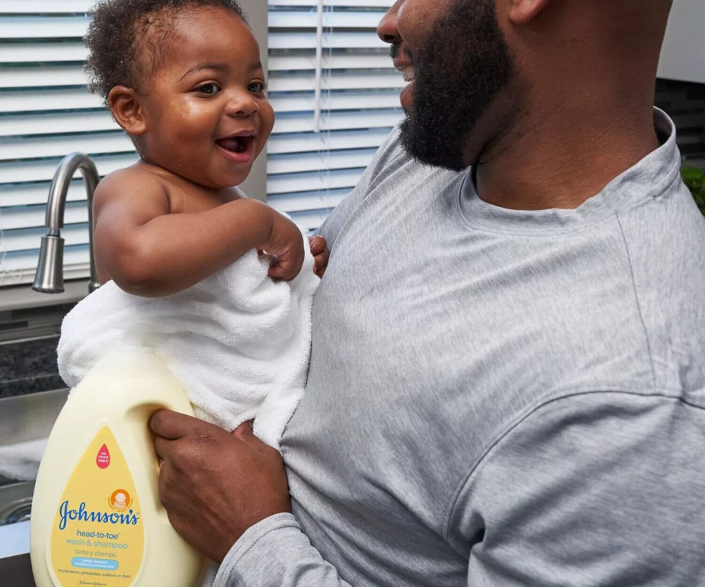 man holding a baby wrapped in a towel and a big bottle of johnson's head to toe baby wash