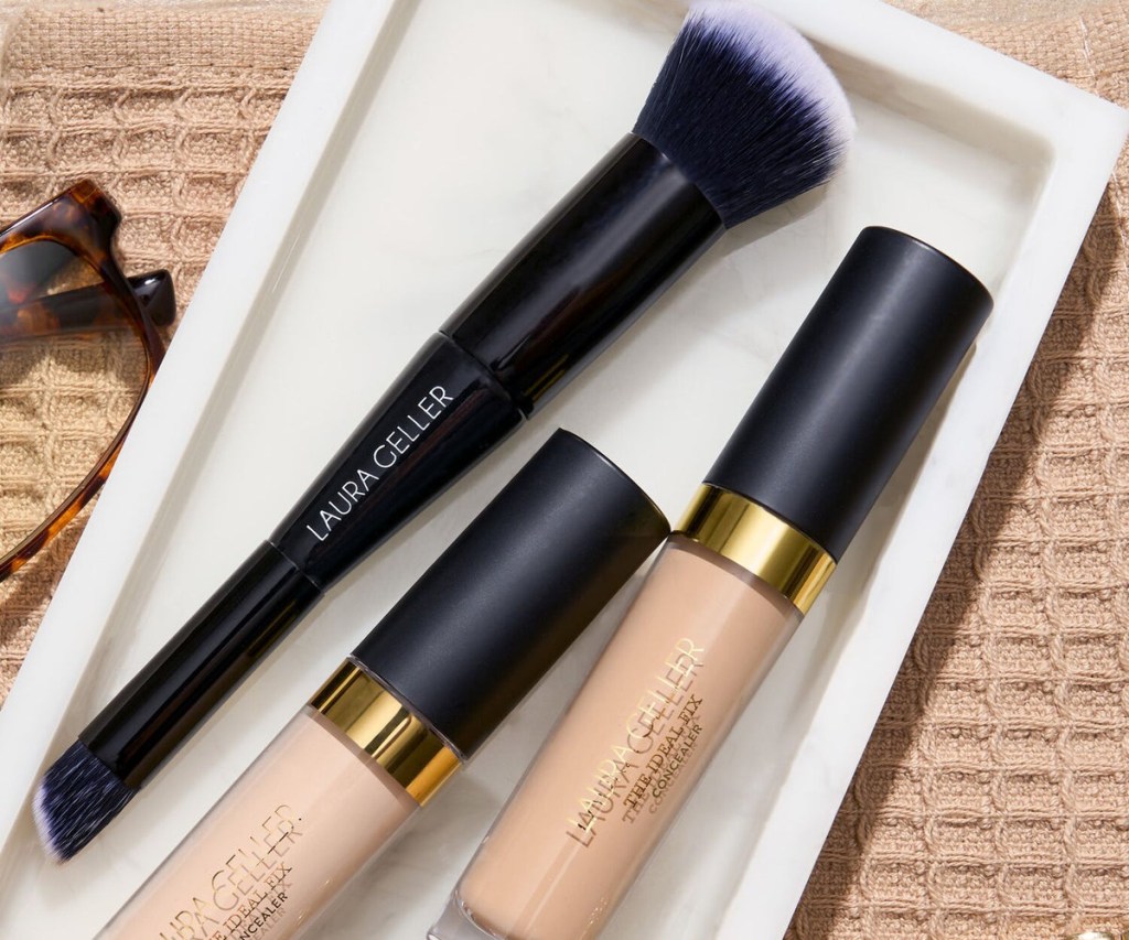 laura geller dual-ended brush next to concealer on a white tray