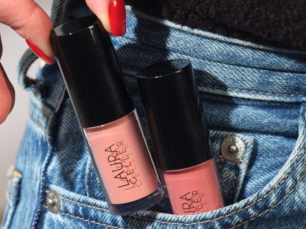 woman with red finger nails putting laura geller lip oils in her jeans pocket