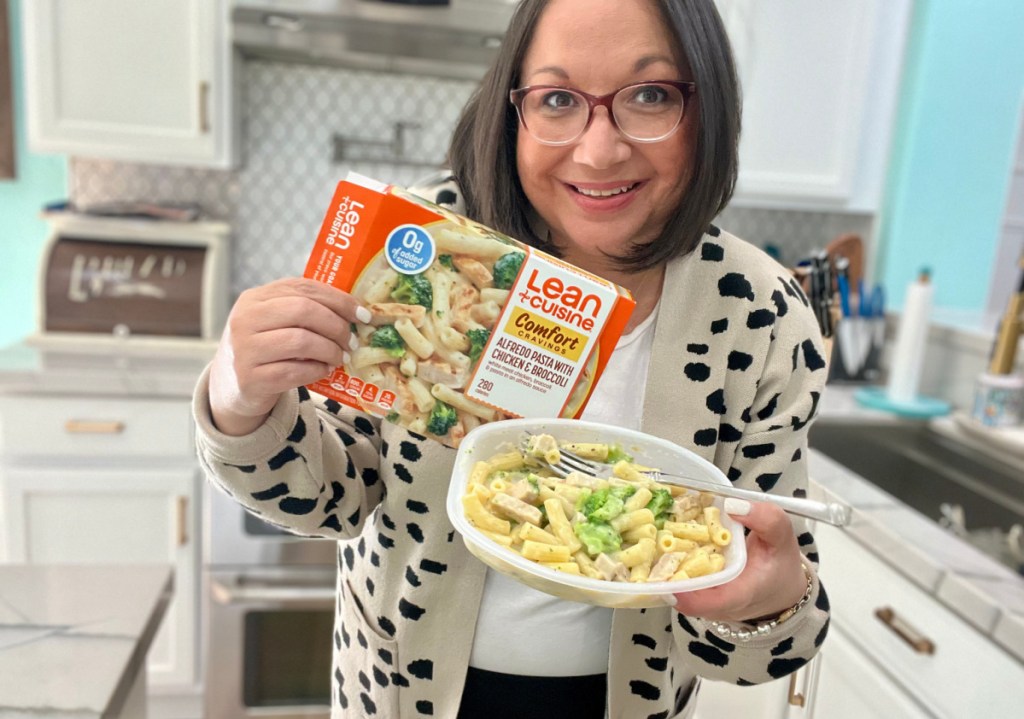 smiling woman standing in a kitchen and holding a cooked lean cuisine pasta meal and the box