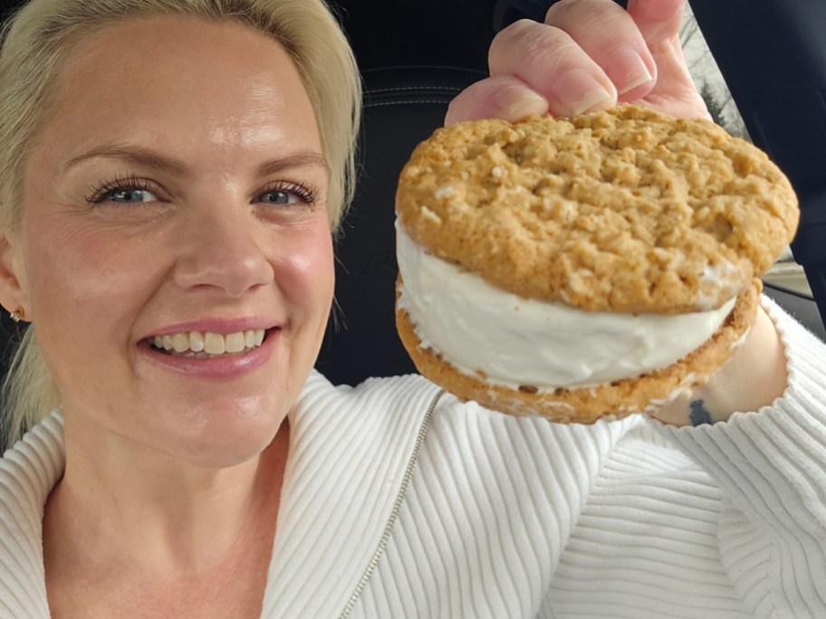 A person smiling and holding a large oatmeal cookie ice cream sandwich.