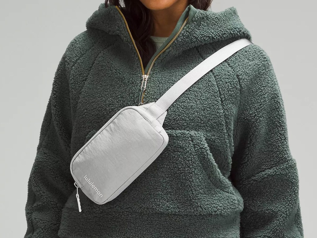 woman in green sherpa jacket with light grey belt bag
