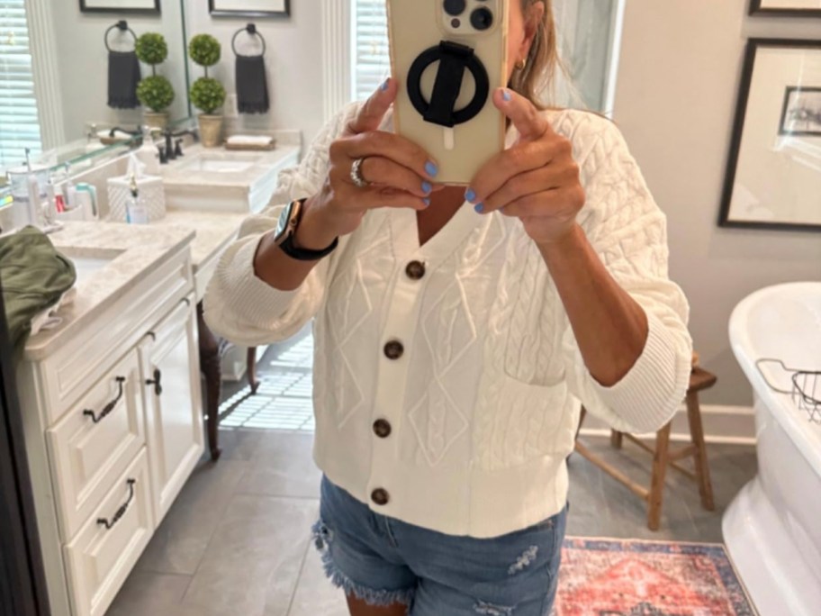 woman taking photo of herself wearing white cardigan in bathroom