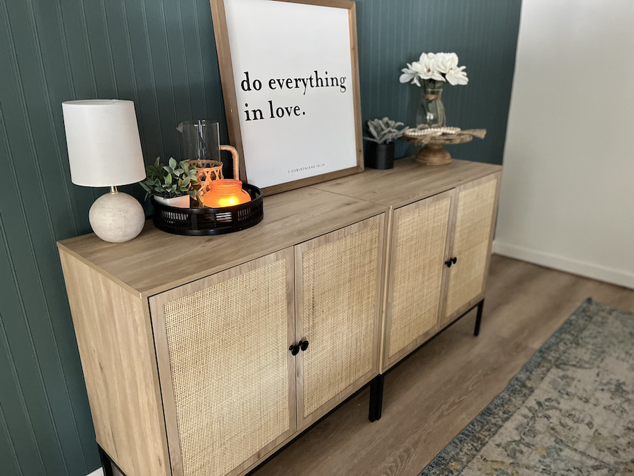 caned sideboard on dark colored wall with art and decor