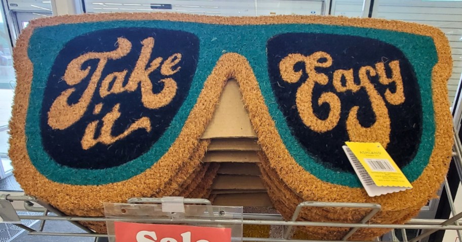 sunglasses shaped coir doormat that says "Take it Easy" on display rack