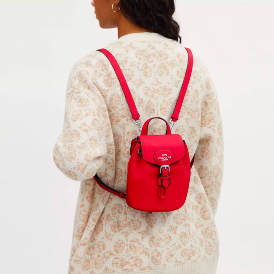 a model wearing a mini red convertible backpack on her back 