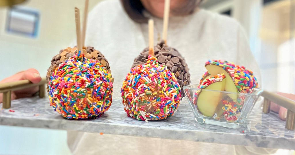 woman holding plate with six chocolate and sprinkle covered apples on it