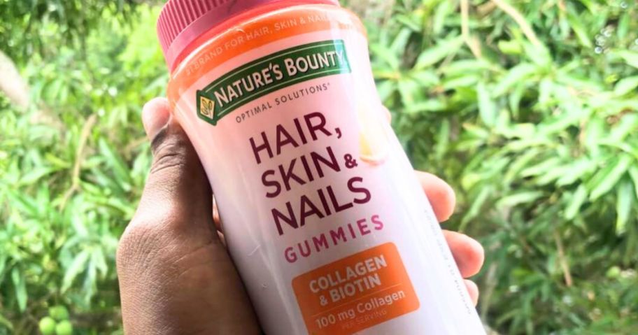 Hand holding a bottle of nature's bounty hair skin and nails gummies