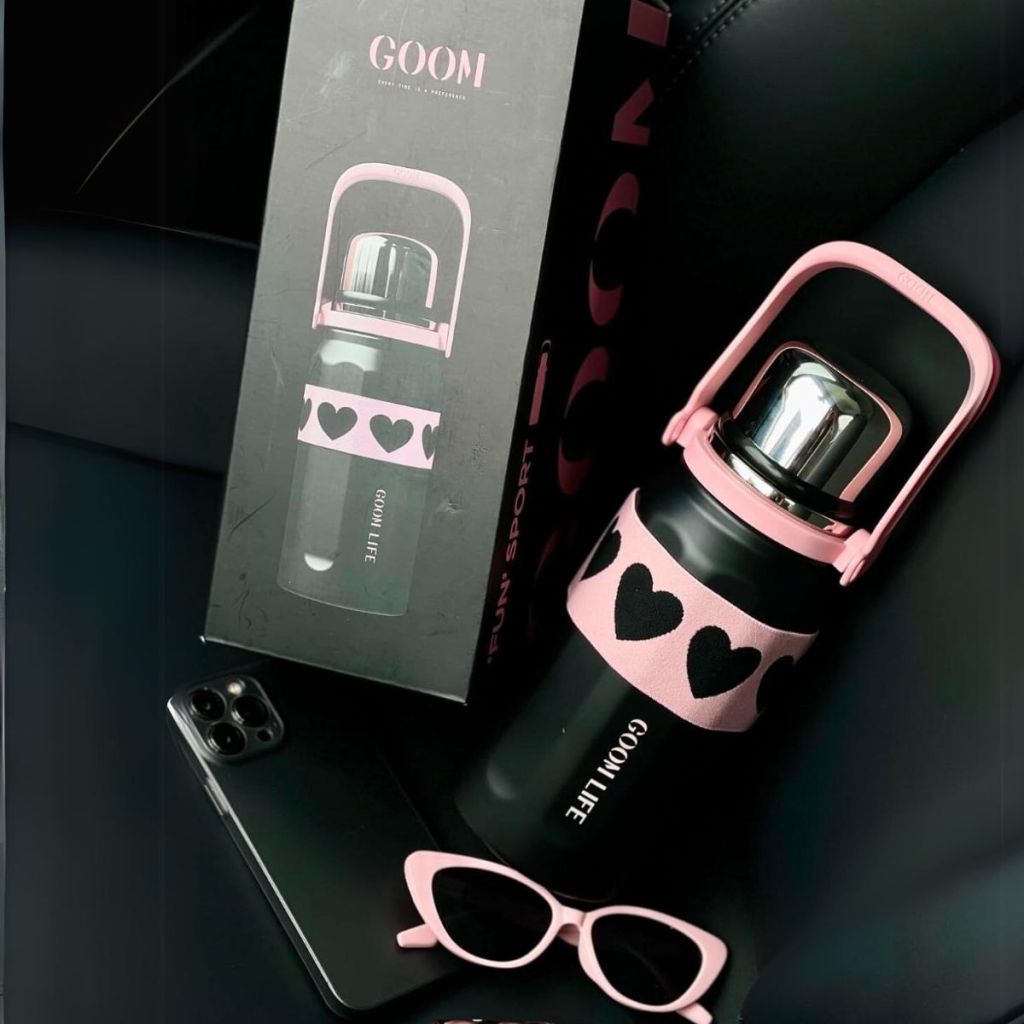 insulated Beverage Thermos with Lid, Flexible Strap, 7-Layer Wide Mouth in black on a car seat next to its packaging and a pair of pink sunnies