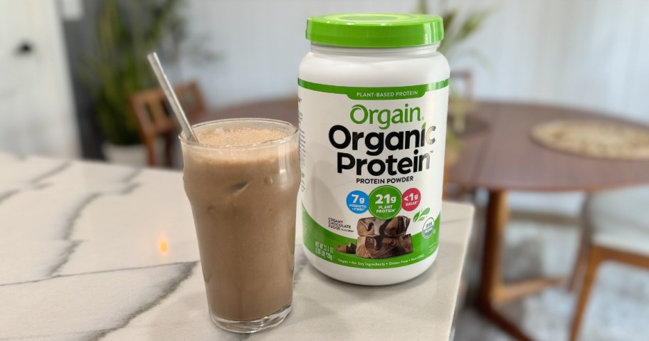 Orgain Organic Vegan Protein Powder large canister on a counter next to a glass of it mixed up