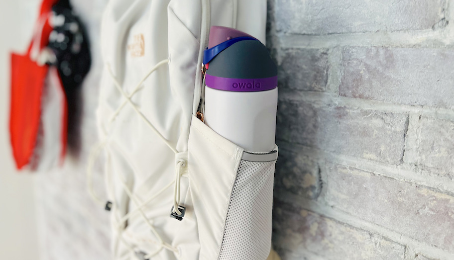 close up of owala water bottle in white book bag hanging on brick wall
