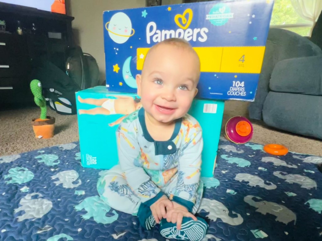 baby sitting in front of pampers diaper boxes