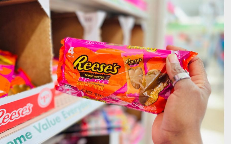 a womans hand grabbing a bag of reeses hearts from a store display