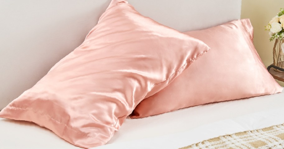 Two pink satin pillowcases on pillows, on a bed.