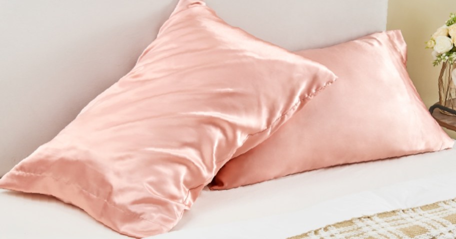 Two pink satin pillowcases on pillows, on a bed.