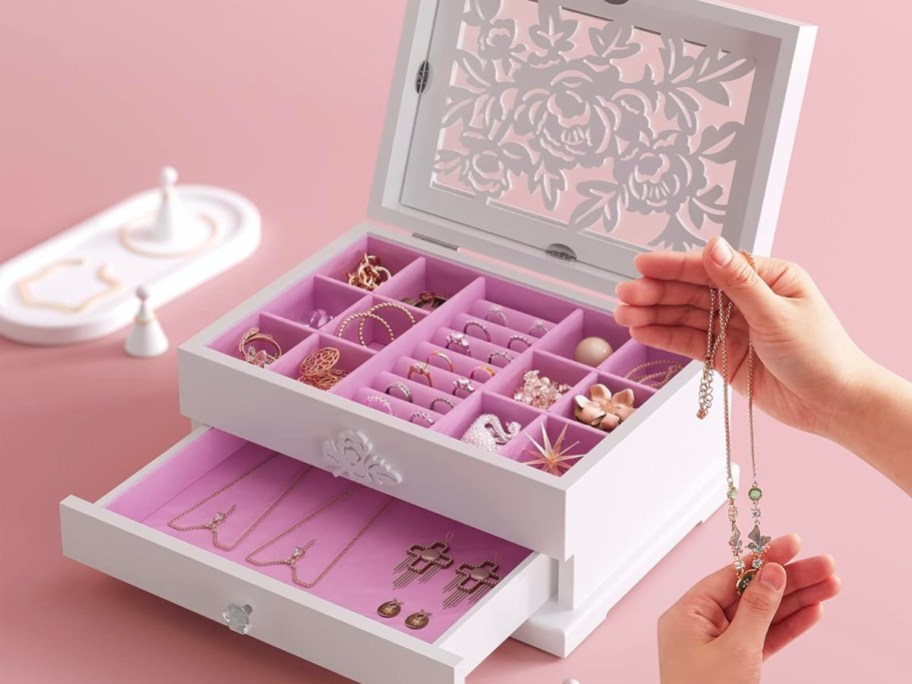 hands taking necklace out of white jewelry box with flower carvings on table
