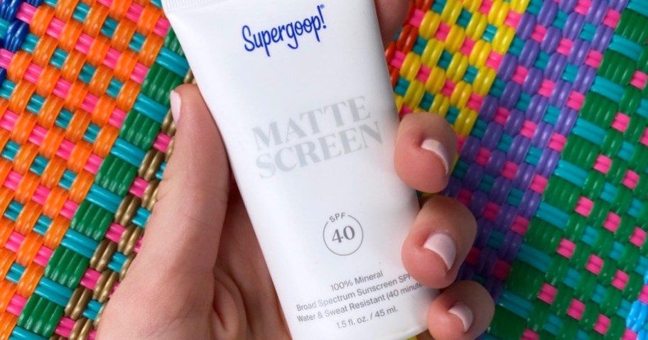 hand holding supergoop mineral sunscreen over multicolored rug