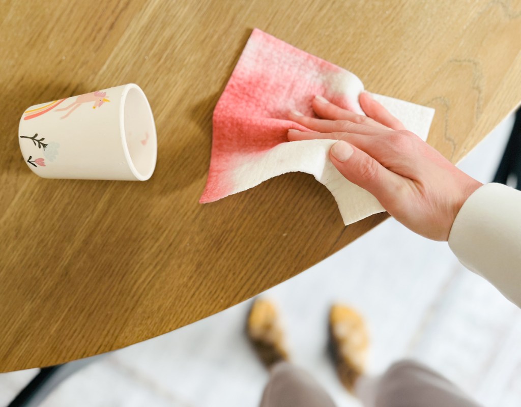 hand wiping wood table with swedish dishcloth