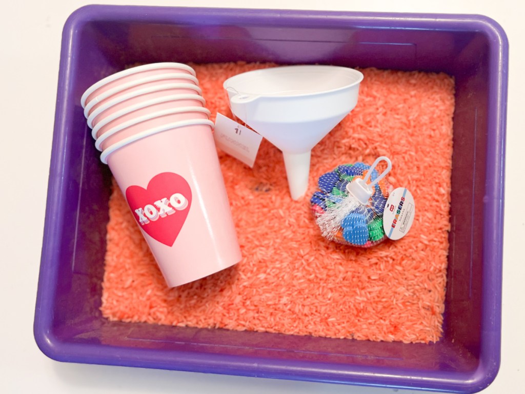 paper cups, funnel, and heart erasers in bin with rice