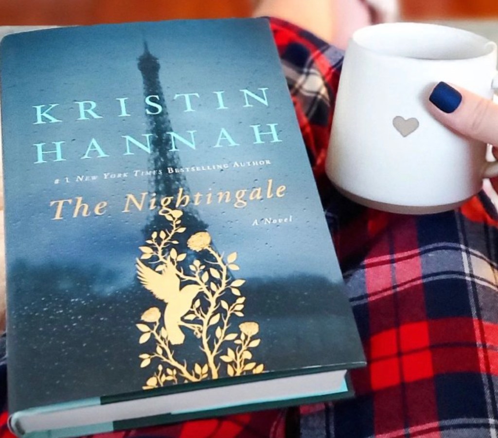 the nightengale book sitting on person's lap with red plaid and white coffee mug with heart