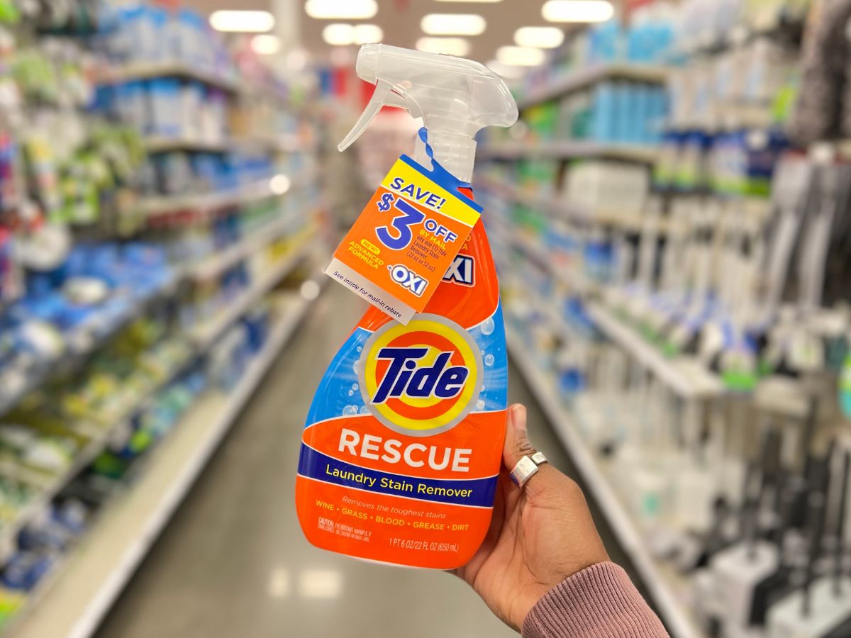 A bottle of tide stain remover being held up in aisle
