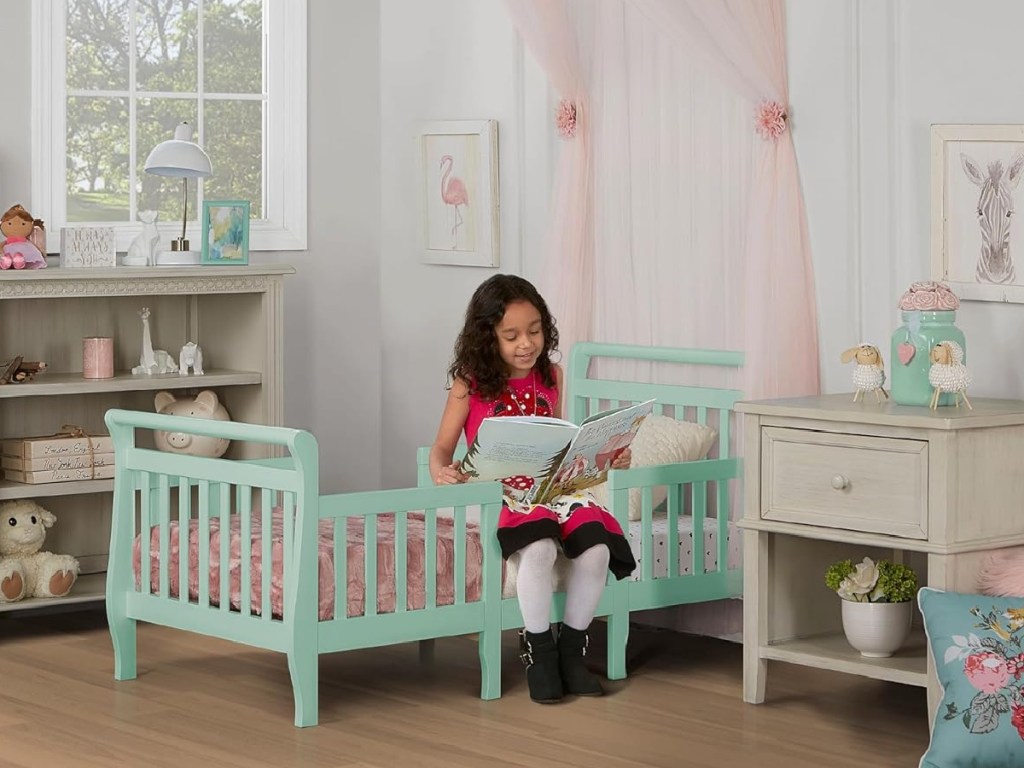 girl sitting on mint colored toddler bed