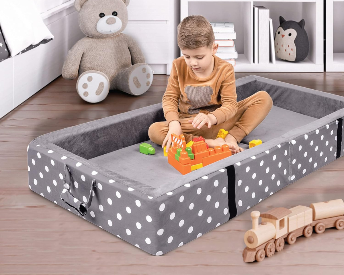 boy sitting in small toddler cot with cozy bumpers