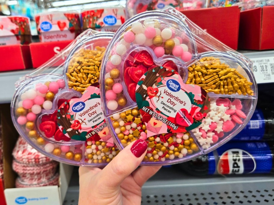 hand holding up two plastic heart shaped containers with Valentine's themed sprinkles and decorations for baking