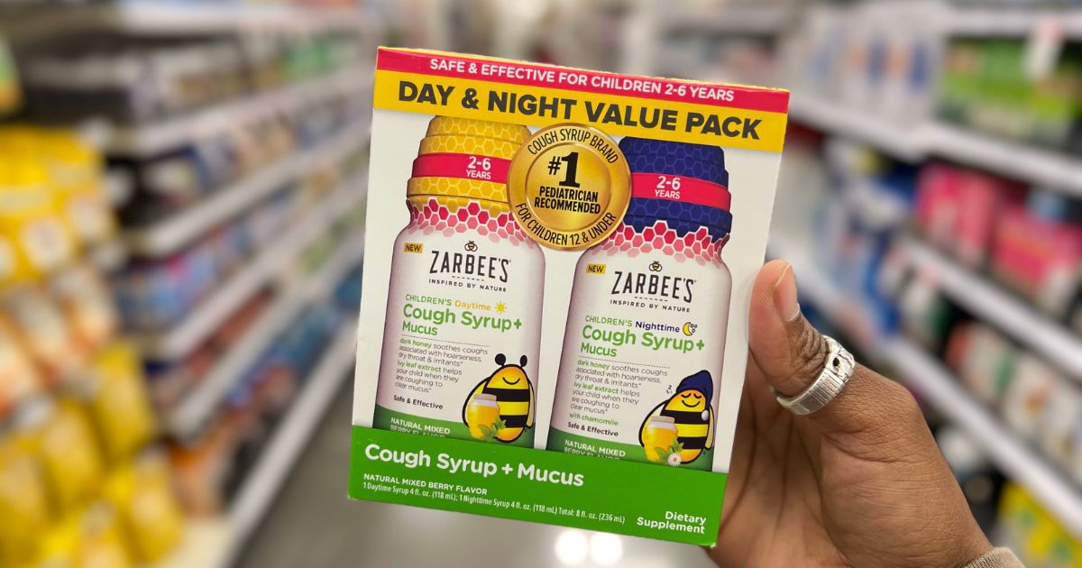 a womans hand holding zarbees day and night cough value back on a store aisle