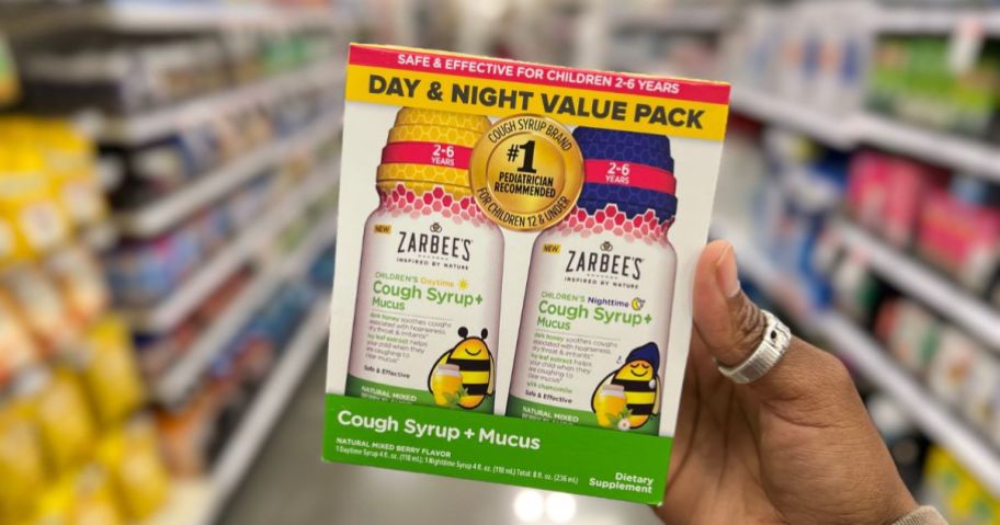 a womans hand holding zarbees day and night cough value back on a store aisle