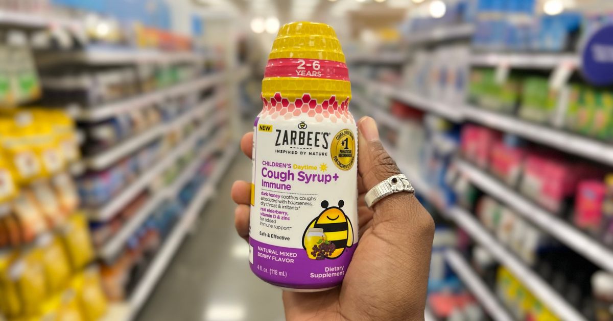 a womans hand holding a bottle zarbees daytime cough syrup and immune support on a store aisle