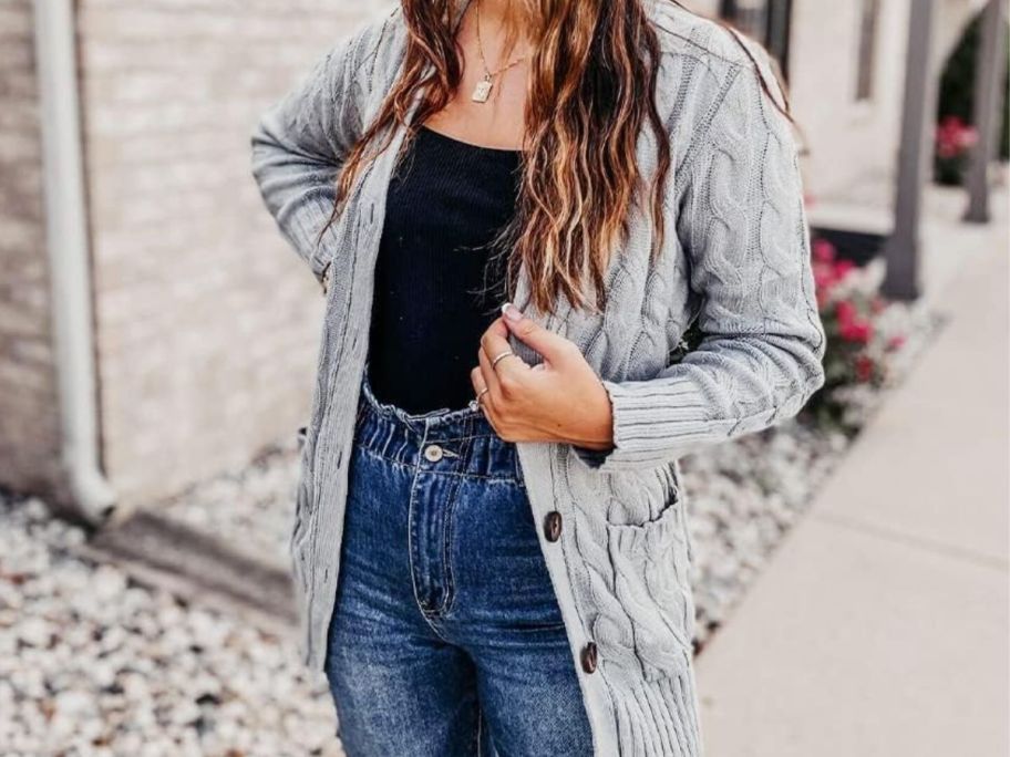 woman standing outside wearing a light grey button down cable knit cardigan