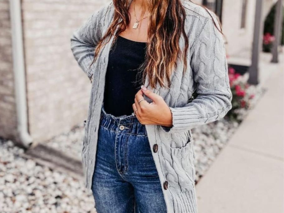 woman standing outside wearing a light grey button down cable knit cardigan