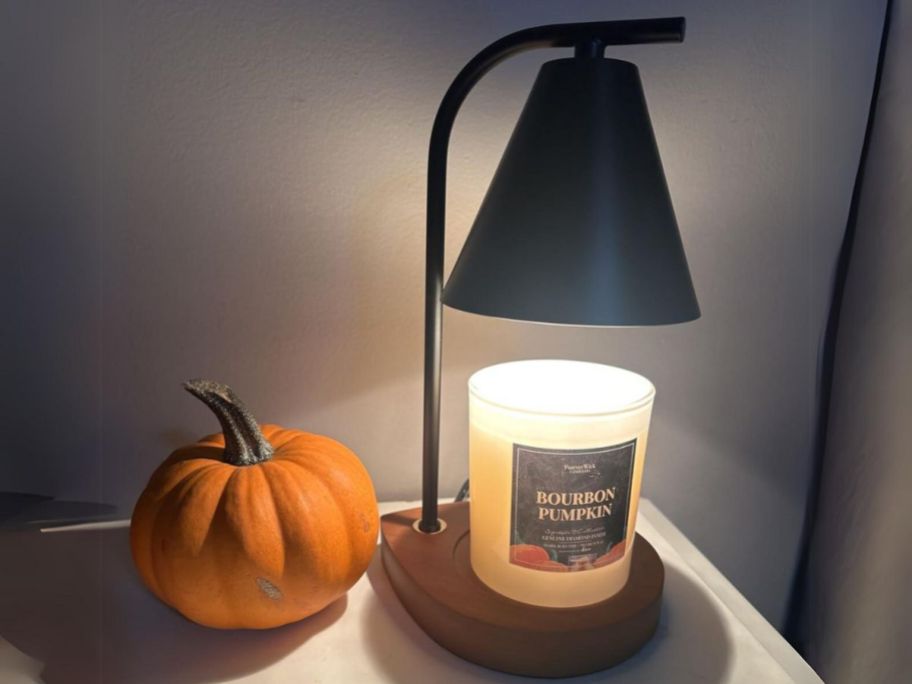 black retro style candle warmer lamp with wooden base lighting up a candle with a pumpkin beside it