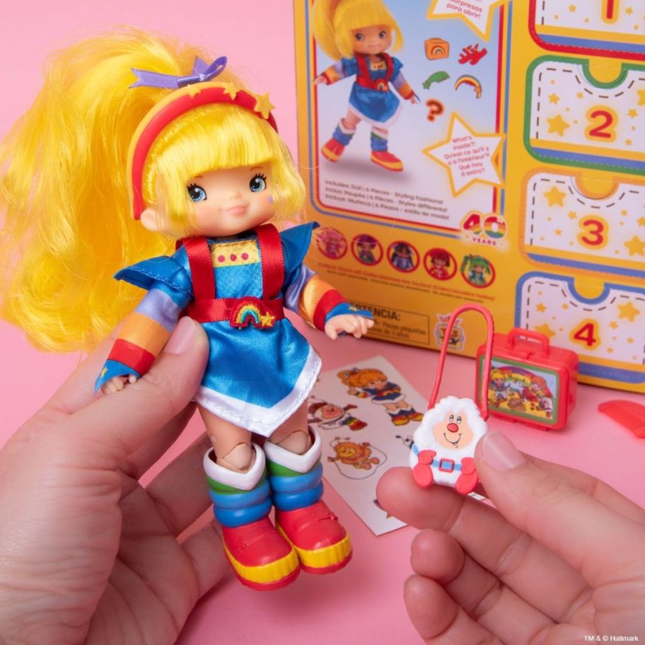 hand holding a small Rainbow Brite doll with accessories, doll box behind it