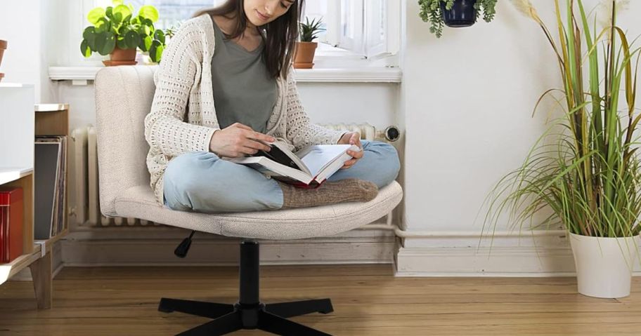 woman sitting cross legged in a beige office chair while reading a book
