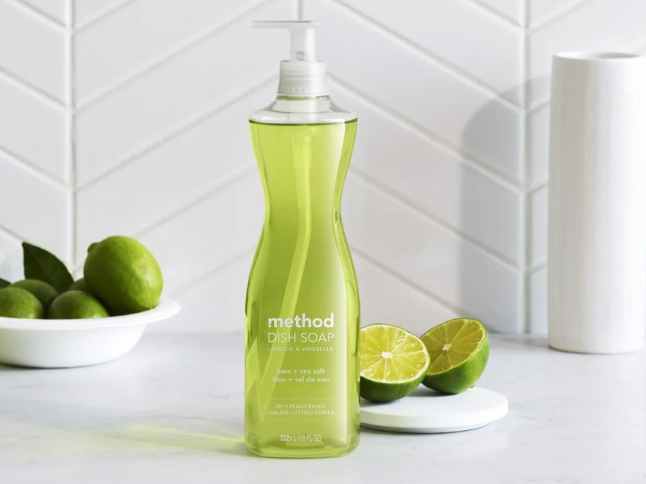 bottle of Method Dish Soap in Lime + Sea Salt on a kitchen counter with limes around it
