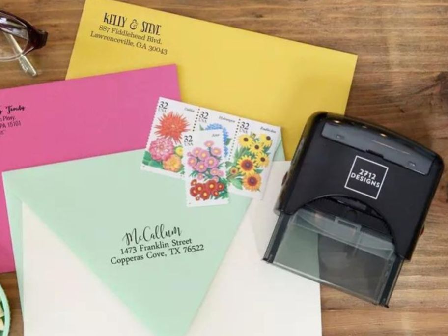 Envelopes with stamps next to a self-inking stamp from 2712 Designs