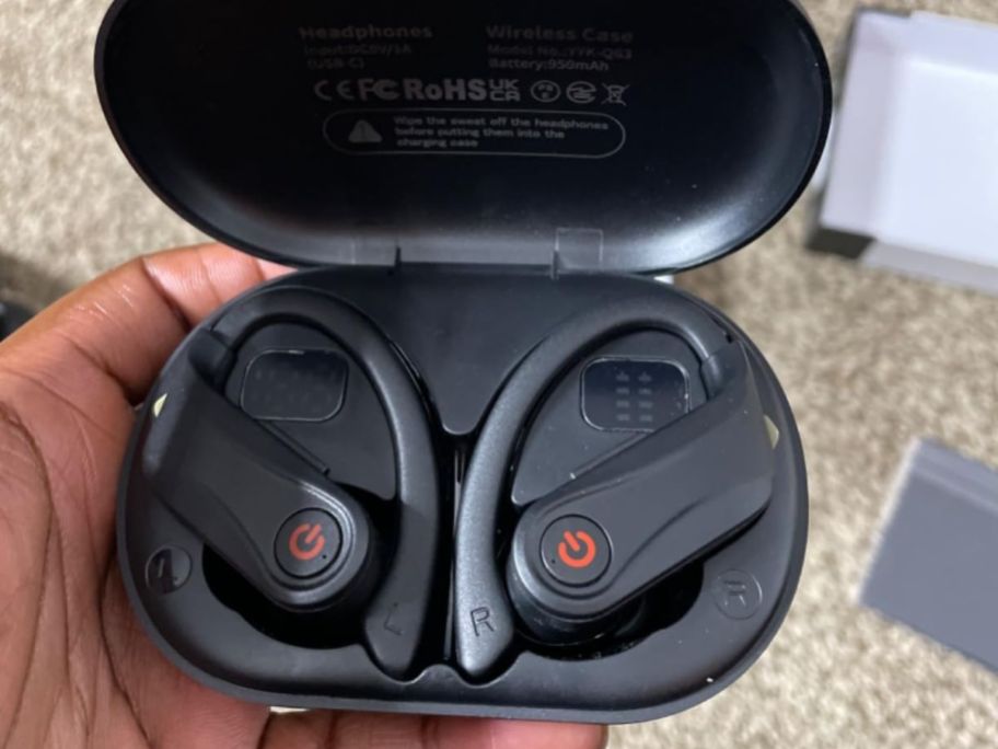 hand holding a pair of black VNMN Wireless Bluetooth Over-Ear Headphones in the charging case