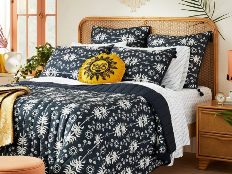 bed with black and white palm frond design comforter, shams and decorative yellow sun pillow