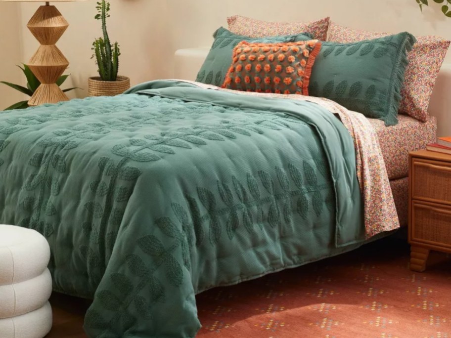 bed with teal green embroidered vine quilt, shams and decorative pillows