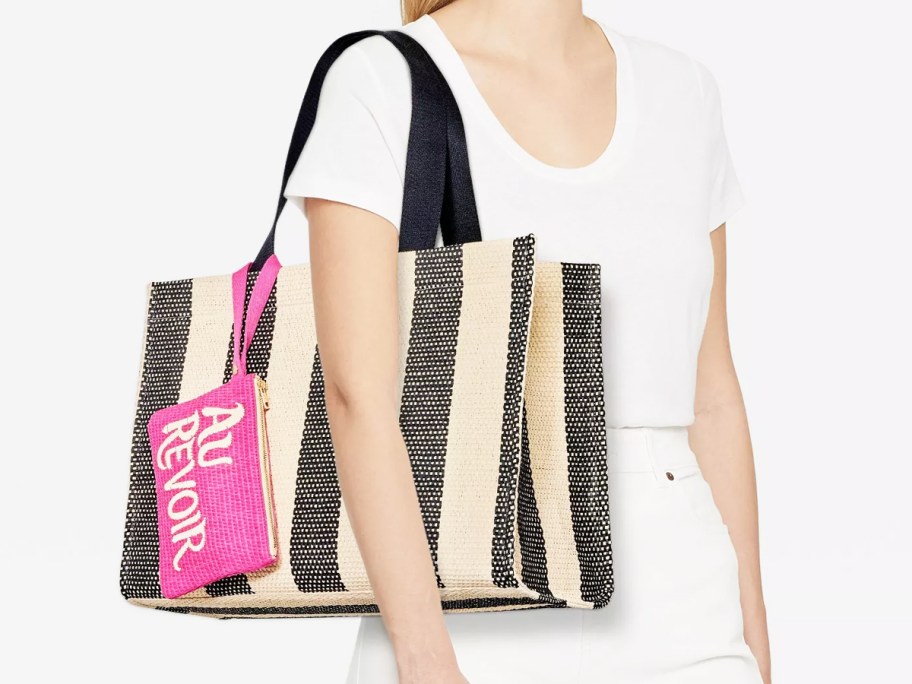 woman with striped tote bag with a small pink pouch that says "au revoir"