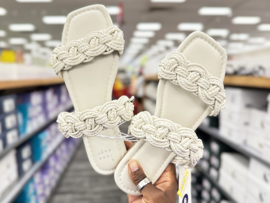 woman holding up a pair of white sandals in store