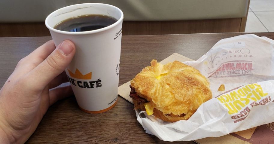 Hand holding a coffee next to a Croissan’wich at Burger King