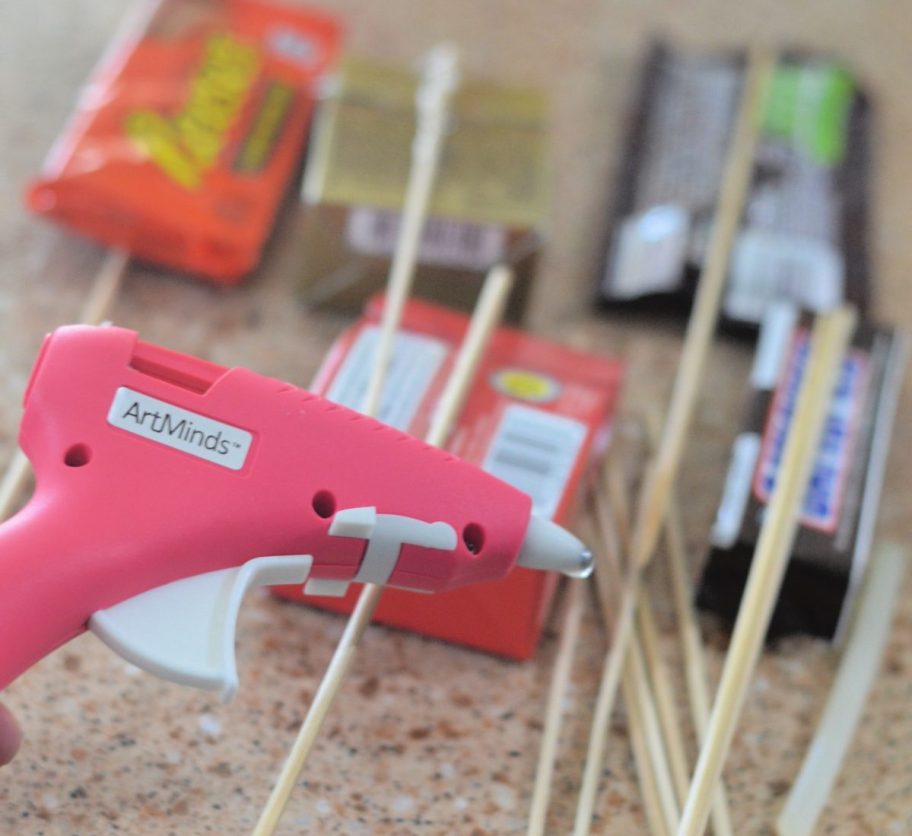 demonstrating how to make a candy bouquet by using a hot glue gun to stick candy to skewers